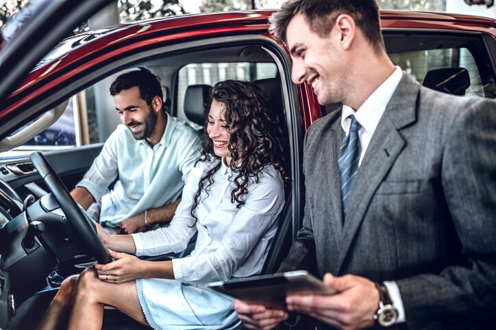 Salesperson showing a new car to a couple after automotive sales training