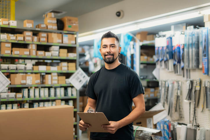 service advisor training graduate standing in auto shop holding clipboard