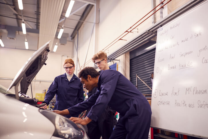 Two students in diesel mechanic training practicing discussing car oil with their instructor during their apprenticeship.