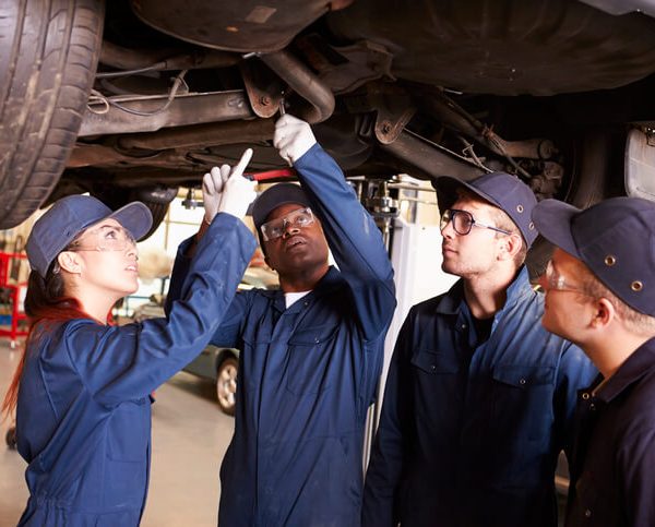 A group of students in diesel mechanic training working as apprentices inspecting under a vehicle.