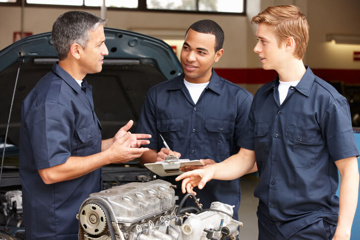 Two students in diesel mechanic training practicing discussing engine repairs with their instructor during their apprenticeship.