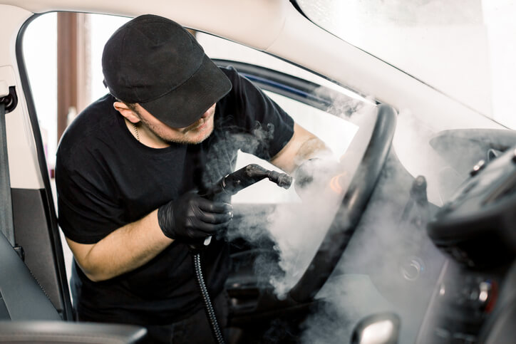 A freelance auto detailer steam treating a car’s dashboard area after auto detailing training.