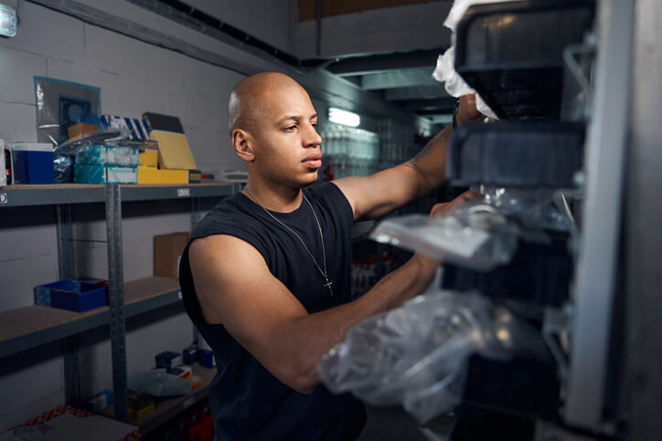 Male auto specialist arranging parts on a shelf after auto parts training.