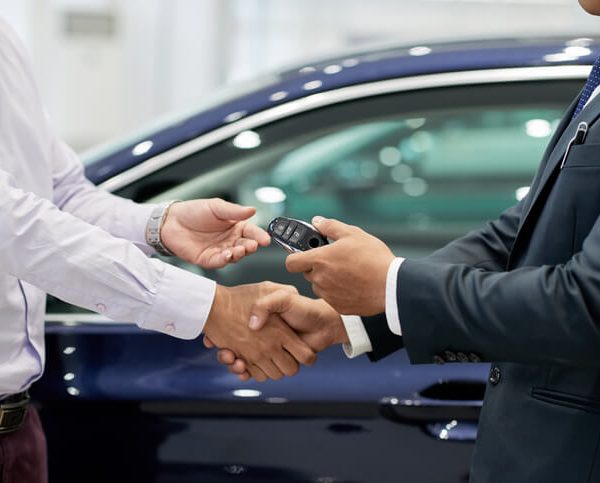 Auto salesman handing over the keys to a new car to a customer after automotive sales training