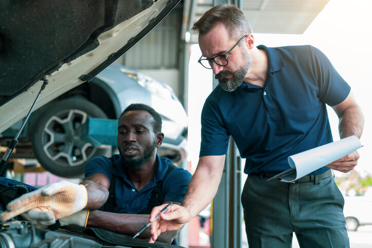 A service advisor with a mechanic at a repair shop confirming a diagnosis after service advisor training.