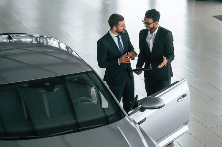 A group of automotive training grads discussing at a car dealership using a tablet