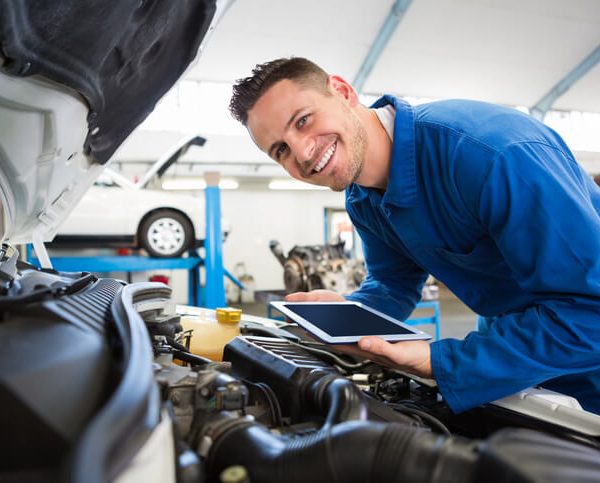 A smiling male auto mechanic using technology to diagnose a car's engine after graduating from auto mechanic school