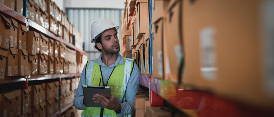 A male warehouse supervisor using a smart tablet to check stock after completing his dispatch training