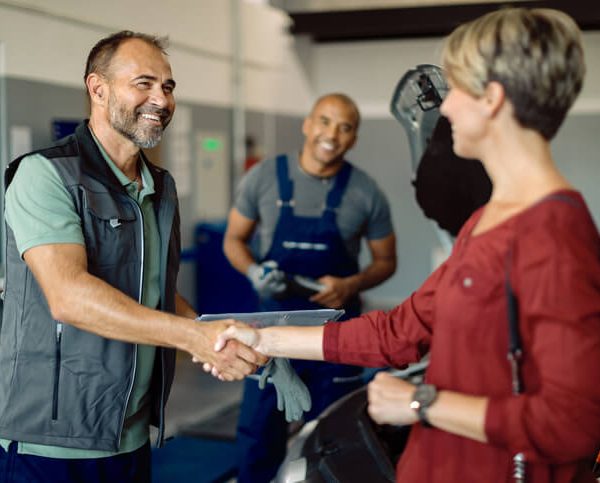 A happy auto mechanic shaking the hands of a female customer after completing his automotive training