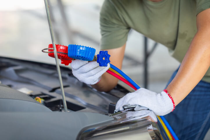 A male climate control specialist checking a vehicle’s refrigerant after automotive air conditioning training