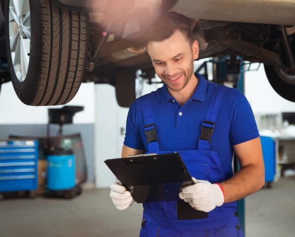 A male auto mechanic with a clipboard in an auto repair shop after completing his auto mechanic training