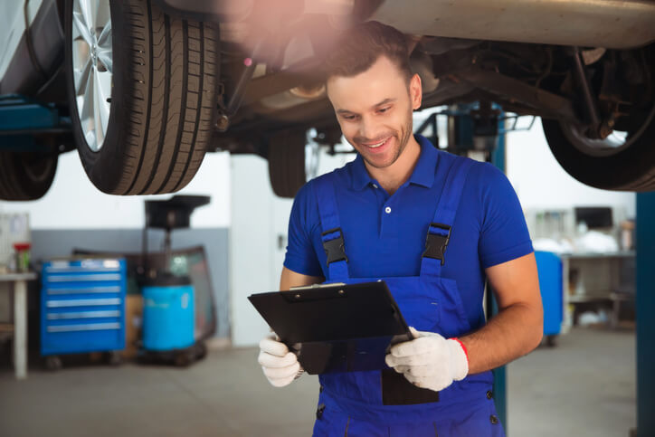 A male auto mechanic with a clipboard in an auto repair shop after completing his auto mechanic training