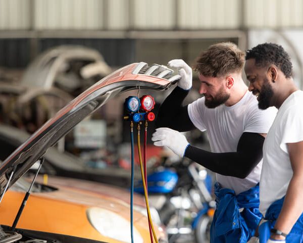 A climate control specialists share a joke while working on a vehicle after their automotive air conditioning training