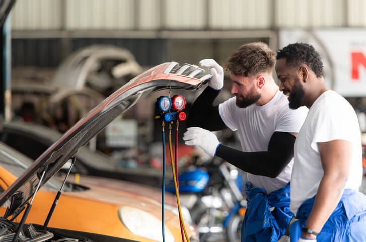 A climate control specialists share a joke while working on a vehicle after their automotive air conditioning training