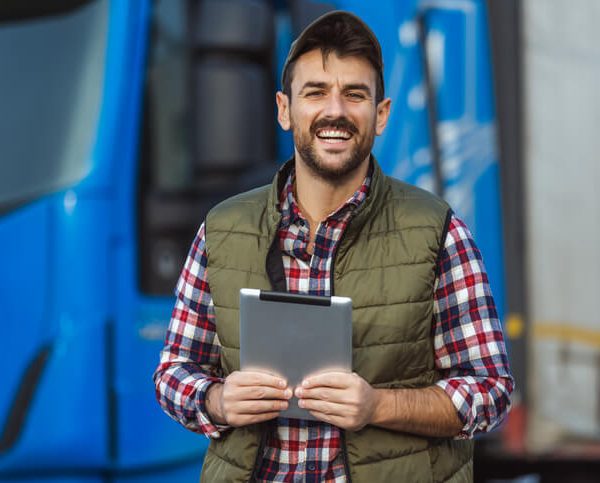 A friendly and confident dispatch manager holding a tablet at a warehouse after completing dispatch college