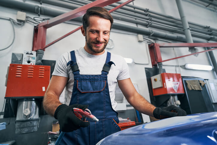 A satisfied mechanic cleaning a repaired car with an air gun after completing auto body technician training