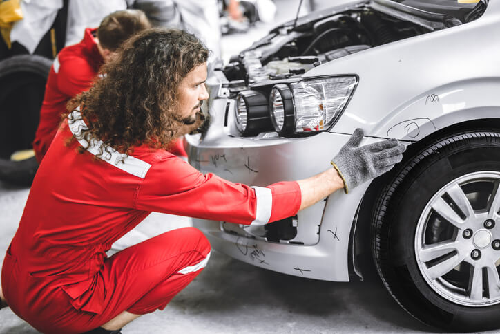 A male auto body technician fixing a damaged car after completing auto body technician training