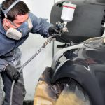 A detailling professional spray painting a car after auto body training