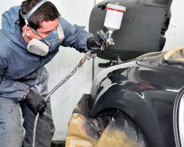 A detailling professional spray painting a car after auto body training