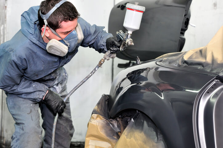 A detailling professional spray painting a car after auto body training