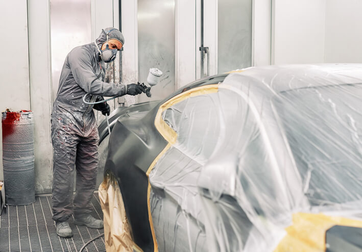 A male auto mechanic painting a car after auto body training