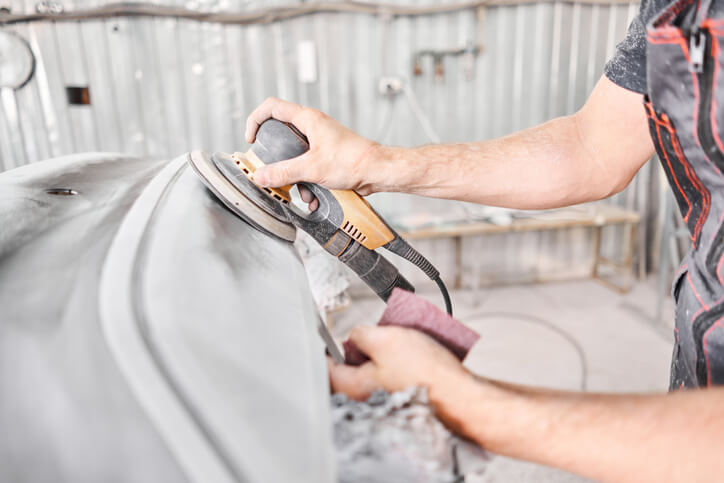 A male mechanic sanding a vehicle using a grinding tool after auto body training