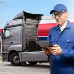 A male log book auditor holding a tablet in front of a truck