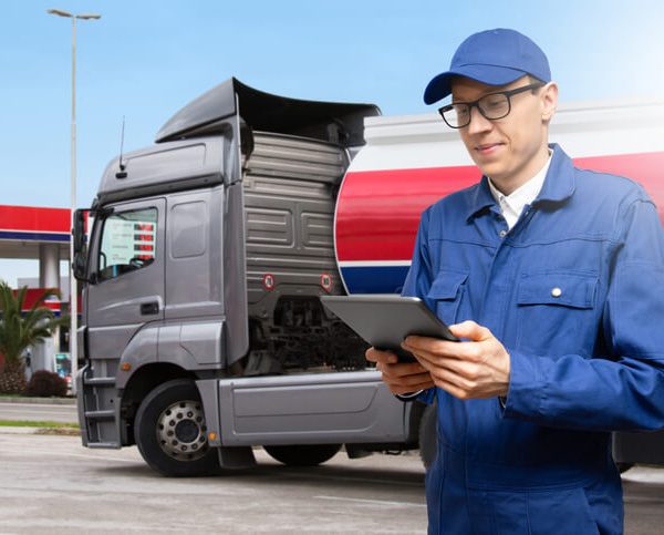 A male log book auditor holding a tablet in front of a truck