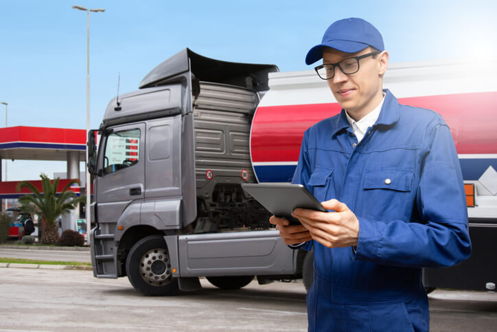 A male log book auditor holding a tablet in front of a truck