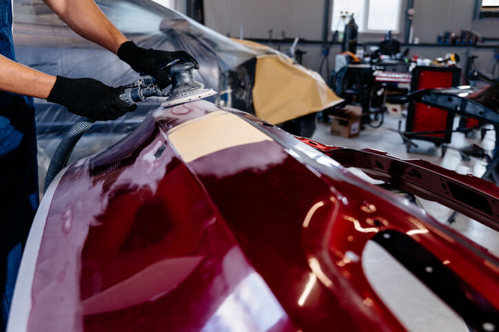 A focused auto mechanic sanding a vehicle body panel at an auto body shop