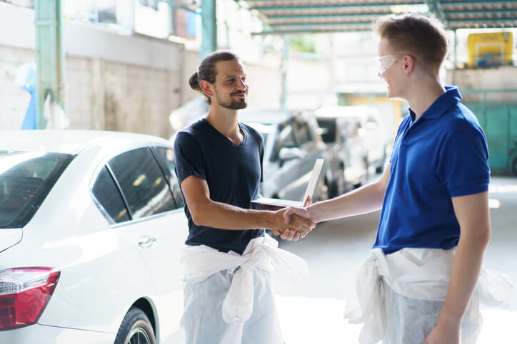 A smiling auto mechanic shaking hands with a satisfied customer at an auto body shop