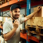 A smiling dispatcher holding a walkie-talkie in a warehouse, using radio language codes learned during dispatch training