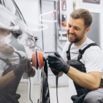 A smiling male auto detailing professional working on a car after completing his auto detailing training