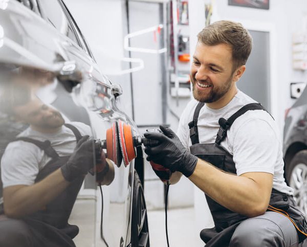 A smiling male auto detailing professional working on a car after completing his auto detailing training