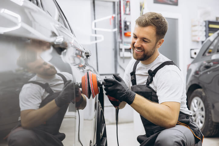 A smiling male auto detailing professional working on a car after completing his auto detailing training