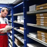 An auto parts specialist reviewing inventory on a tablet in a warehouse after completing his auto parts training.