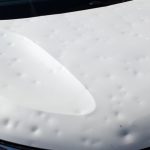 A close-up of a dented car hood affecting aerodynamics, to be explored in auto body training.