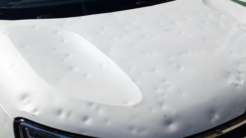 A close-up of a dented car hood affecting aerodynamics, to be explored in auto body training.